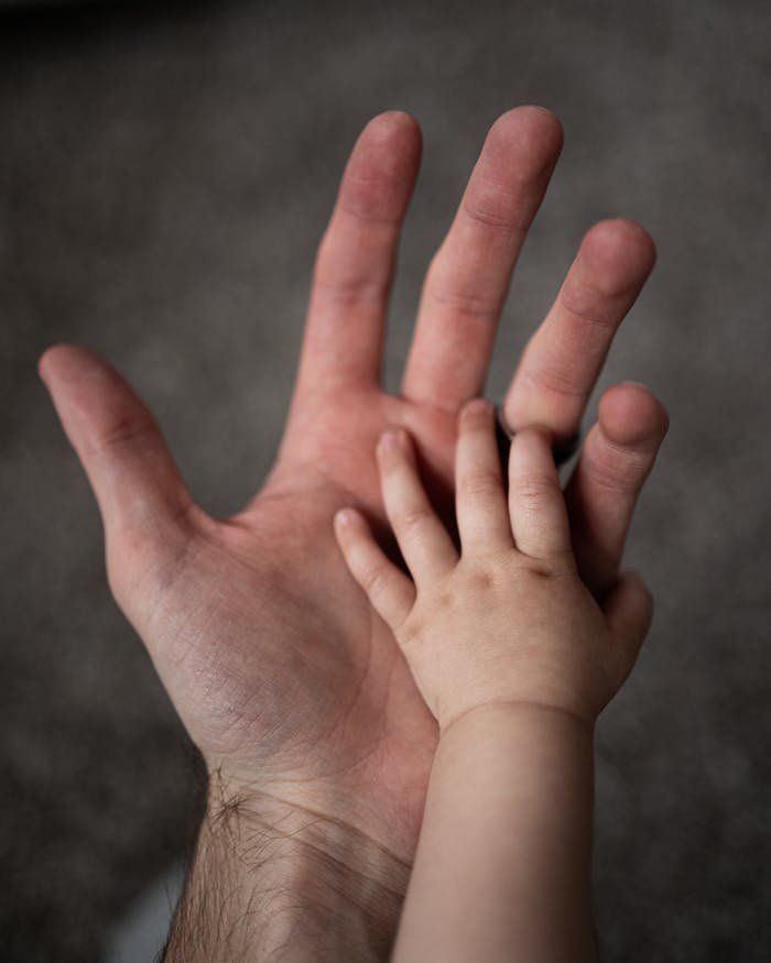 Close-up of a father's hand gently holding his baby's hand, symbolizing love and care.
