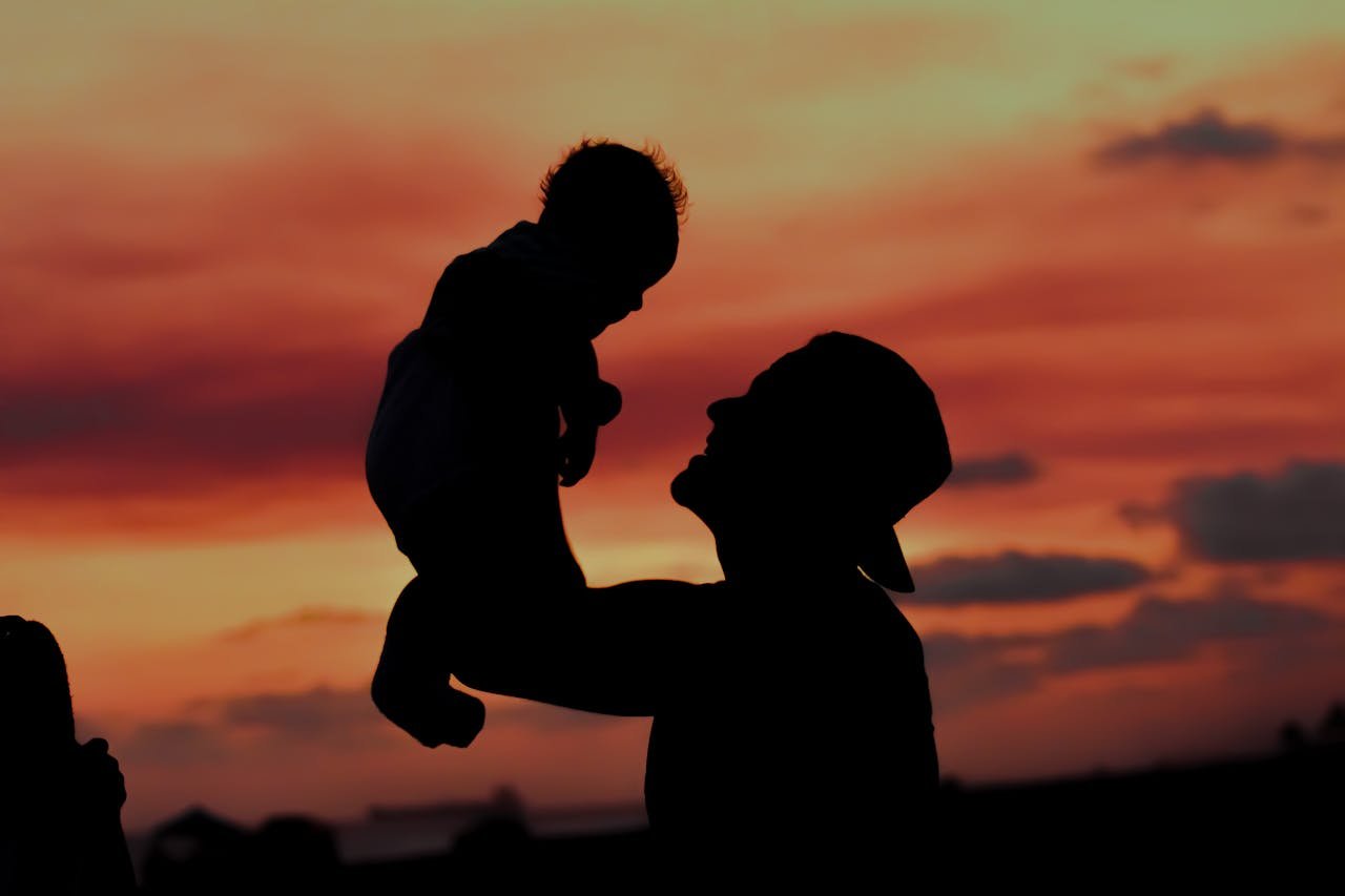 A beautiful silhouette of a father lifting his child against a vibrant sunset sky, symbolizing love and family bond.
